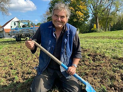Mann kniet auf dem Acker und hält einen Spaten in der Hand.