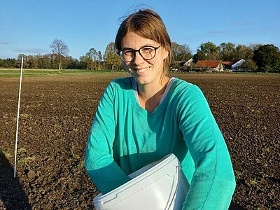 Frau hält einen weißen Eimer im Arm und greift mit der Hand hinein.